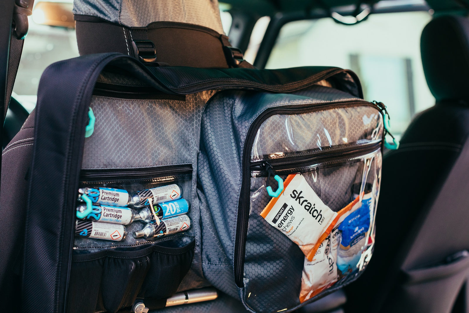 Top half of Parc cycling gear bag hanging in car on headrest using Parcs innovative headrest hood. Cycling gear and nutrition is seen in the clear pockets.