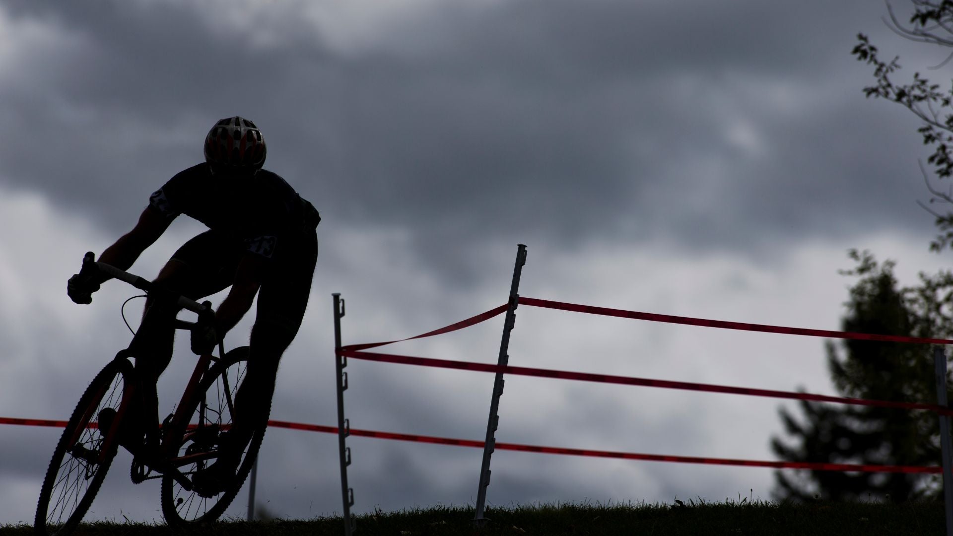 cyclocross racer navigates a turn on their bike in front of dark clouds