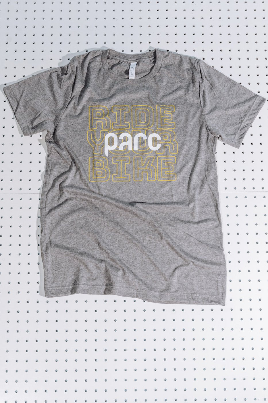 Parc model standing outside wearing grey short sleeve t-shirt. T-shirt illustration on the front chest shows the words ride your bike stacked in a yellow outlined font with a white parc logo over the top.