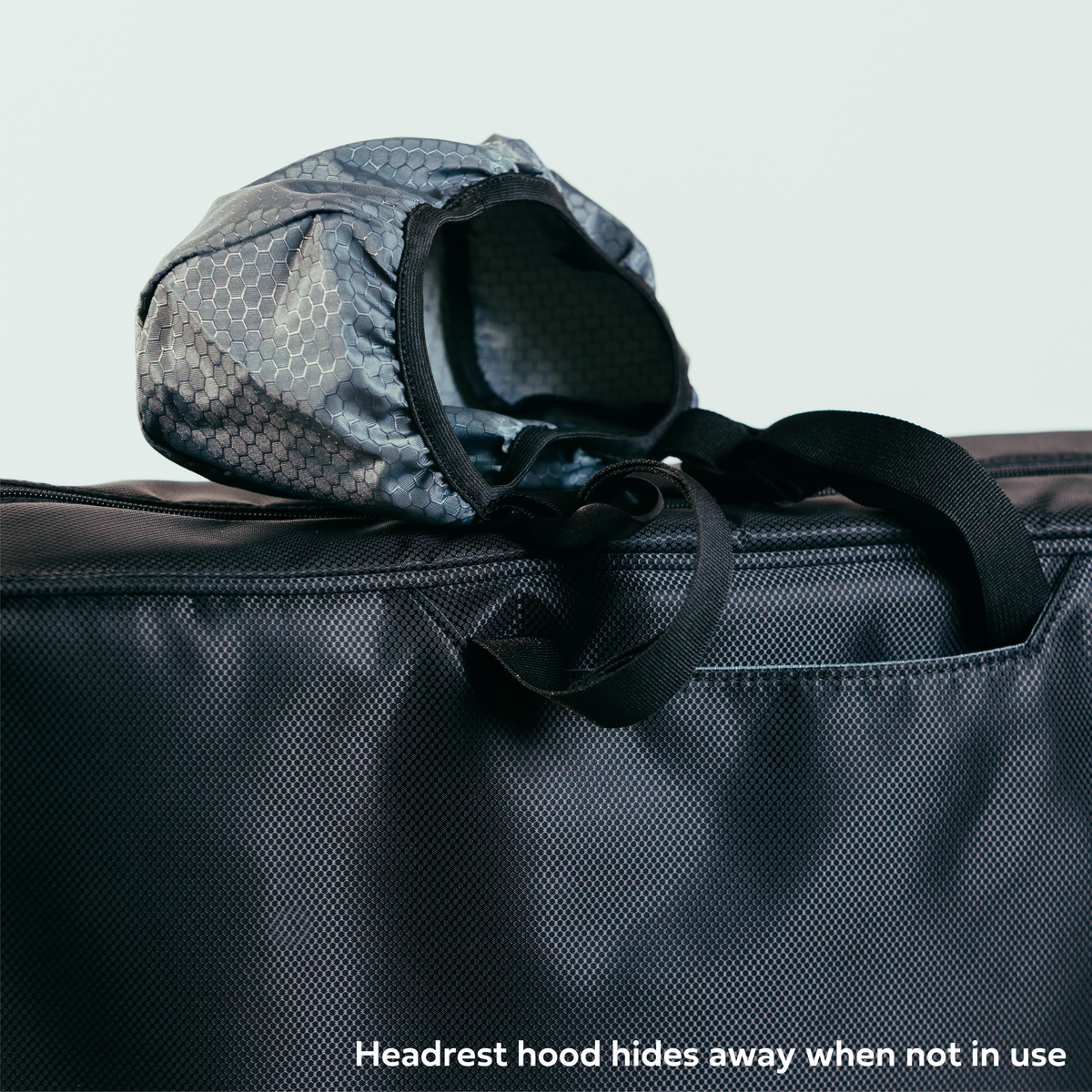 Close up view of Parc’s innovative car headrest hood sticking out of its dedicated pocket with velcro closure. Headrest hood is grey ripstop material with black webbing adjustable straps. Text on photo says headrest hood hides away when not in use.