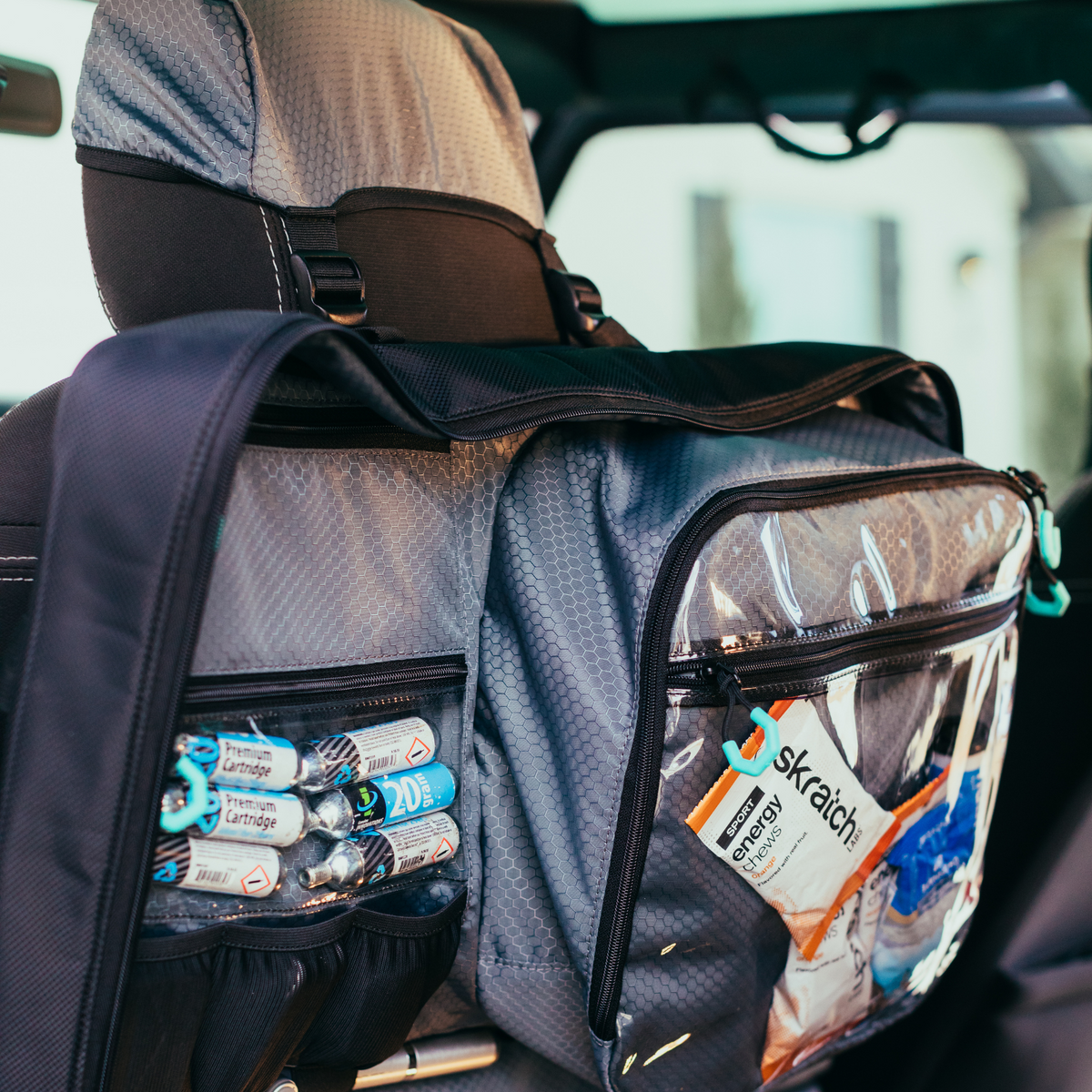 The Bag by Parc, a cycling gear bag, hanging on a car headrest from The Bags innovative hideaway headrest hood. Top half of the bag shown, full of cycling gear and cycling kit.