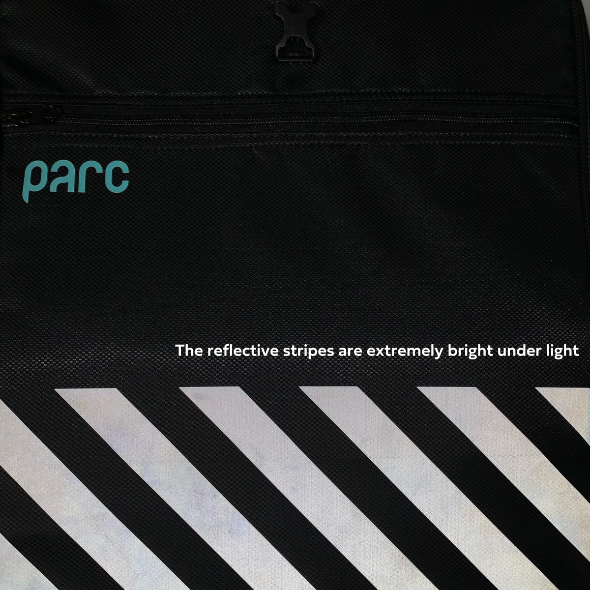 Close up view of exterior of Parc cycling gear bag showing reflective stripes glowing under light in dark. Normally black stripes appear bright white under light. Parc turquoise logo visible on cycling kit bag.